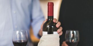 Dwie osoby piją czerwone wino przy stole, butelka owinięta w płótno