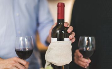 Jak serwować wino do wegańskiej kolacji: praktyczne połączenia smaków i gotowe inspiracje Dwie osoby piją czerwone wino przy stole, butelka owinięta w płótno
