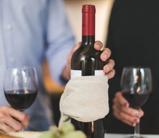 Dwie osoby piją czerwone wino przy stole, butelka owinięta w płótno